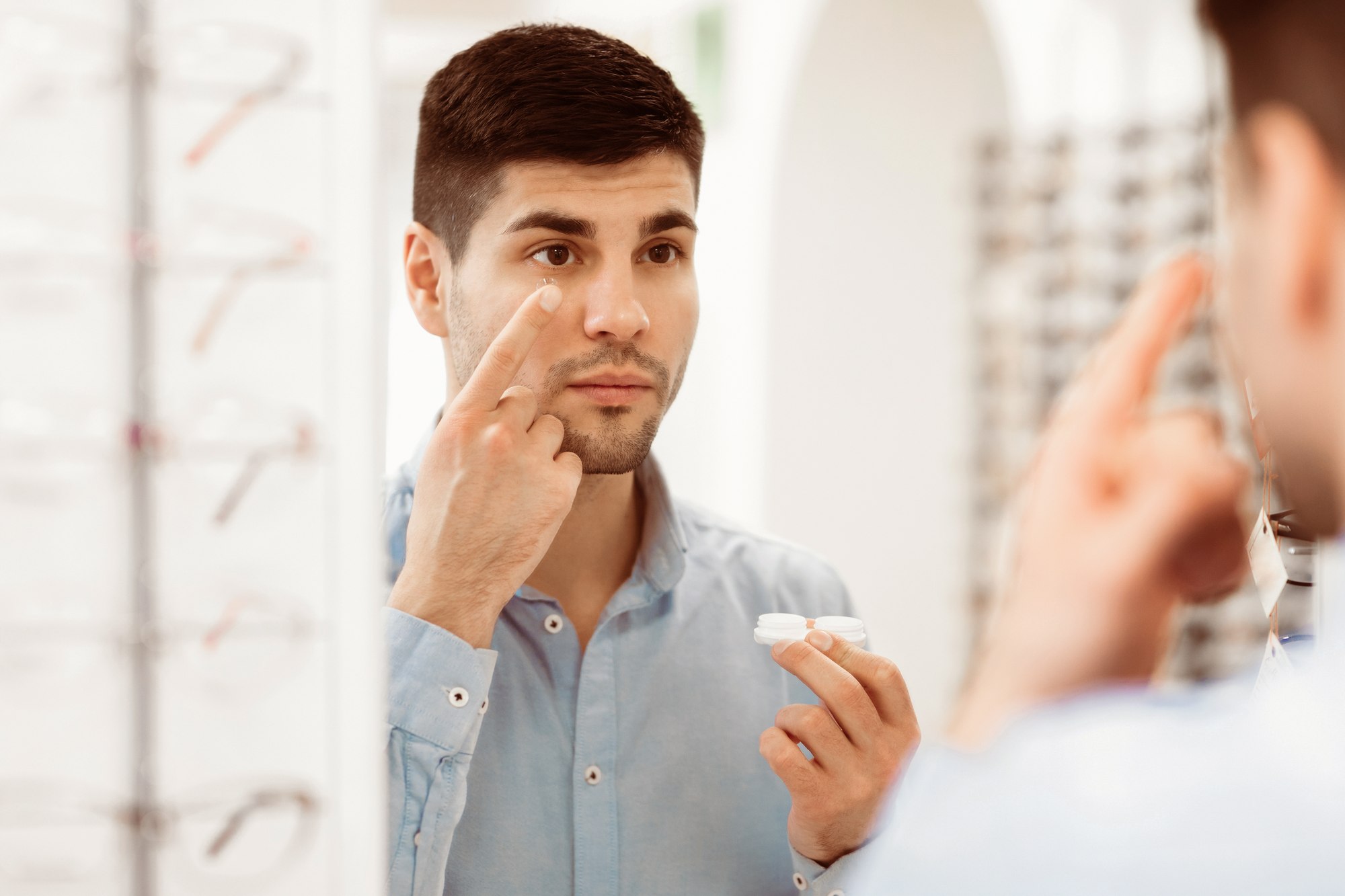 A man inserting a contact lens in front of a mirror